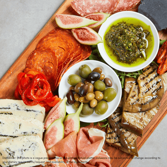 Wooden charcuterie board with bread, cheese, salami, olives, and crackers on a wooden surface.